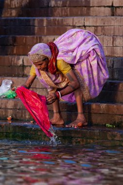 Mor elbiseli yaşlı bir kadın Ganj Nehri 'nin kutsal sularında tekstil yıkıyor. Varanasi, Hindistan