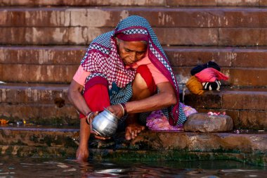 Renkli elbiseli yaşlı kadın Ganj Nehri 'nin kutsal sularında gümüş kavanozunu yıkıyor. Varanasi, Hindistan