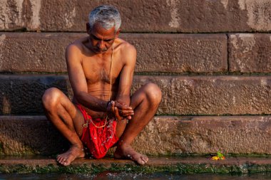 Ganj Nehri 'nin kıyısında oturan yaşlı adam. Varanasi, Hindistan