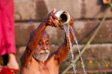 Ganj Nehri 'nin kutsal sularına gümüş kavanozdan su döken yaşlı adam. Varanasi, Hindistan