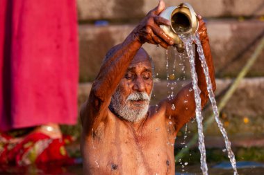 Ganj Nehri 'nin kutsal sularına gümüş kavanozdan su döken yaşlı adam. Varanasi, Hindistan