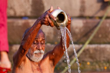 Ganj Nehri 'nin kutsal sularına gümüş kavanozdan su döken yaşlı adam. Varanasi, Hindistan