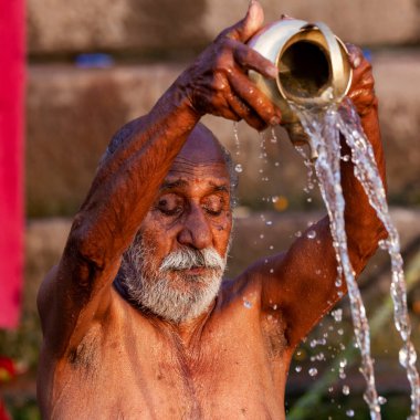 Ganj Nehri 'nin kutsal sularına gümüş kavanozdan su döken yaşlı adam. Varanasi, Hindistan