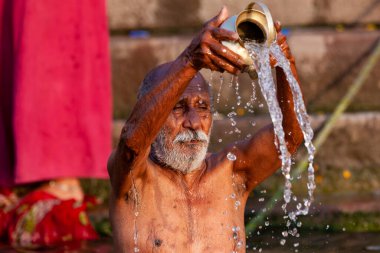 Ganj Nehri 'nin kutsal sularına gümüş kavanozdan su döken yaşlı adam. Varanasi, Hindistan