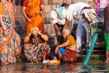 Erkekler kadınların kafalarını tıraş eder ve Ganj Nehri 'nin kutsal sularının yanında otururlar. Varanasi, Hindistan