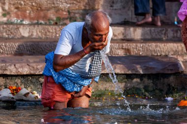 Yaşlı bir adam kendini yıkıyor ve Ganj Nehri 'nin kutsal sularını içiyor. Varanasi, Hindistan