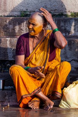 Sarı yüzlü kel bir kadın oturuyor. Varanasi, Hindistan