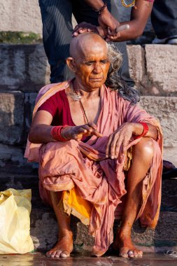 Ganj Nehri 'nin yanında yaşlı kadının kafasını tıraş eden adam. Varanasi, Hindistan