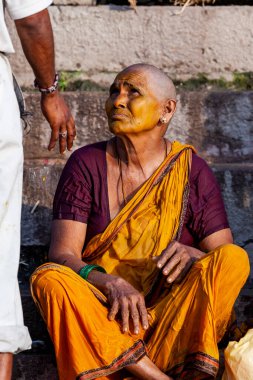 Sarı yüzlü kel bir kadın oturuyor. Varanasi, Hindistan