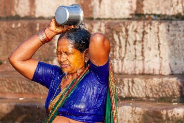 Kimliği belirsiz yeşil elbiseli kadın Ganj nehrinden gelen suyla kendini gümüş kavanozdan yıkıyor. Varanasi, Hindistan