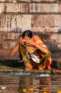 Renkli elbiseli bir kadın Ganj Nehri 'nin suyuyla yüzünü yıkıyor. Varanasi, Hindistan 