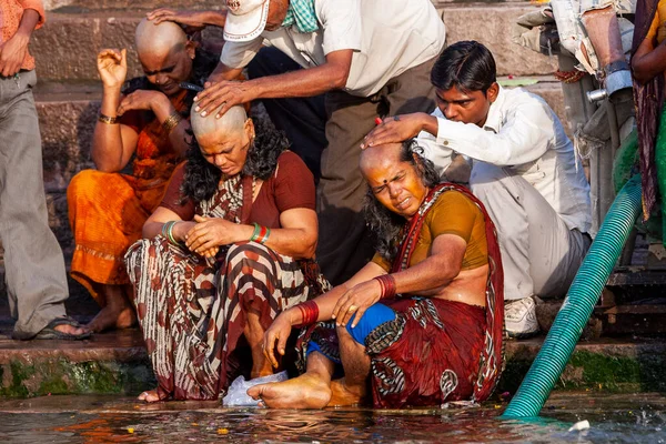 男性は女性の頭を剃り ガンジス川の神聖な水の横に座っている インドのバラナシ — ストック写真