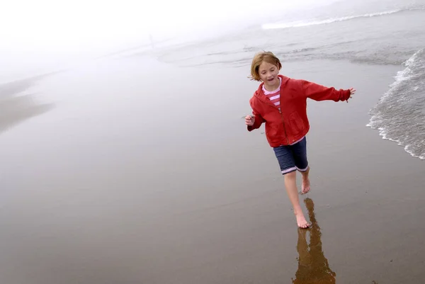 Gadis Kecil Pantai Berkabut Mengenakan Jaket Merah Dan Celana Pendek — Stok Foto