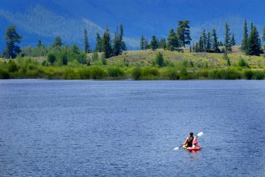 Göl dağlarındaki kayaktaki adam vahşi doğada kürek çekiyor.