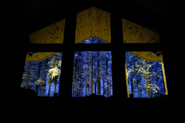 Cabin windows looking out into the dark at snow covered forest in winter