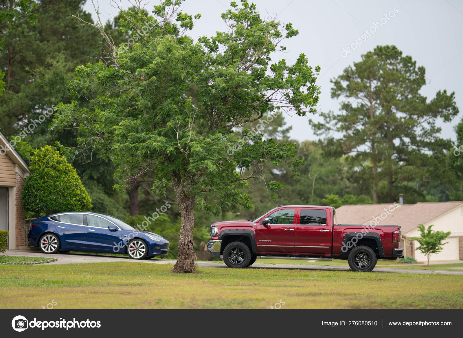Driveway With Tesla Model 3 Electric Car And Red Lifted Pick