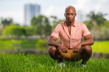 Gras üzerinde çömelmiş yakışıklı bir genç Afrikalı-Amerikalı adam fotoğrafı