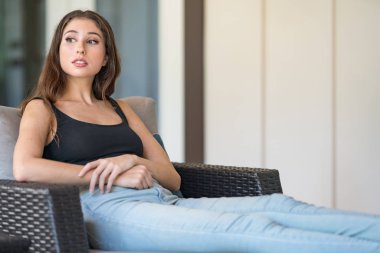 Çekici genç kadın hasır sandalyede poz ve uzağa bakıyor