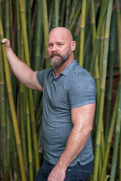 Guapo adulto modelo masculino posando en un jardín de bambú mirando c — Foto de Stock