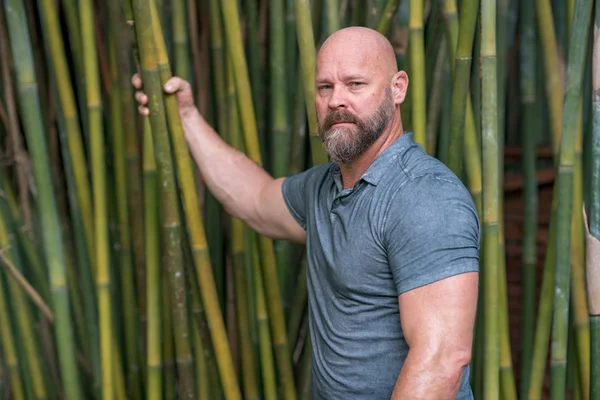 Hombre posando en jardín con brazo sobre plantas de bambú borrosas en la ba — Foto de Stock