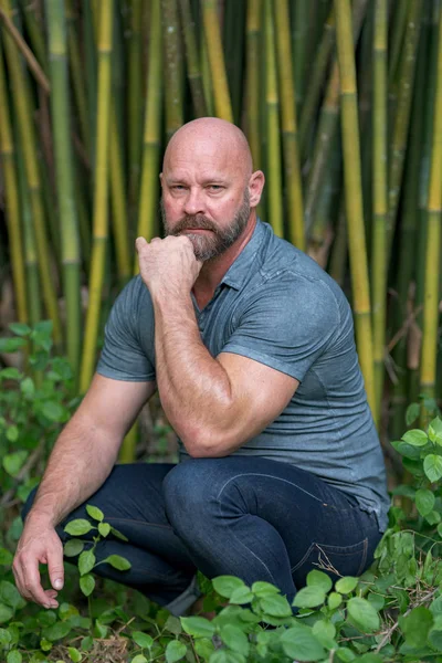 Handsome macho man posing on a bamboo background. Male model bal — Stock Photo, Image