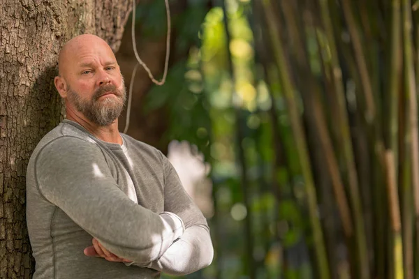 Macho uomo con le braccia incrociate appoggiato su un albero — Foto Stock