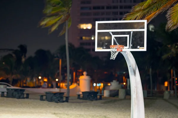 Basketball hoop in a park at night with palm trees and tables Fo — Stock Photo, Image