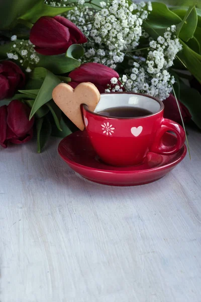 桌子上有红郁金香和一杯带饼干心的茶 — 图库照片