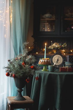 Mumlarla süslenmiş Noel pastası, peri ışıkları ve Noel ağacının yanındaki şenlik masasında hediyeler. Sıcak Noel atmosferiyle sıcak bir tatil evi.