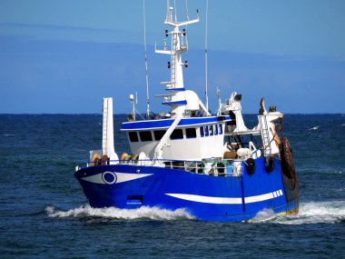 Blue fishing vessel underway at speed heading to fishing grounds. clipart