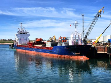 Coastal cargo ship discharging cargo at harbour berth facilities. clipart