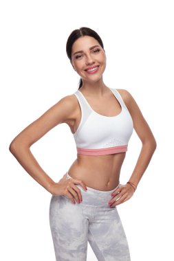 gülümseyen ve ellerle kalça üzerinde beyaz bir arka plan üzerinde duran seksi esmer fitness kadın