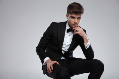 Açık gri renkli, metal sandalye üzerinde oturan siyah smokin düşünceli zarif genç adam bir altın yüzük parmağı üzerinde sahip portresi