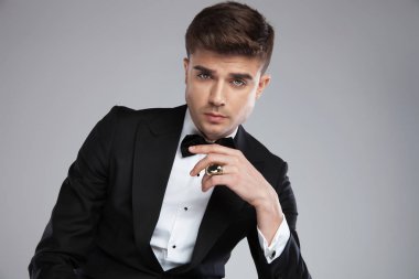 seksi işadamı parmağındaki hafif gri arka plan üzerinde oturan altın yüzük ile siyah bir smokin giyiyor seductively seyir portresi