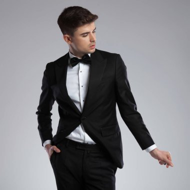 seksi bir adam portresi resmen parmaklarını yapışma giymiş ve yan cebinde el ile ışık gri arka plan üzerinde dururken isteyen, rahat seyir