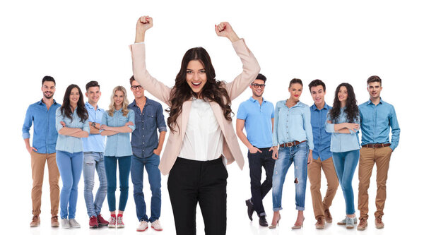 Празднование лидера команды бизнесвумен стоя перед ее победителем случайная группа с обеими руками в воздухе, глядя взволнованно, на белом фоне
