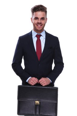 Lacivert takım elbiseli yakışıklı işadamı duran siyah bir evrak çantası beyaz arka plan üzerinde tutar.