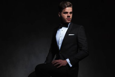 Smokin tarafına siyah arka plan üzerine el uyluk dinlenme süre seyir oturan zarif adam portresi