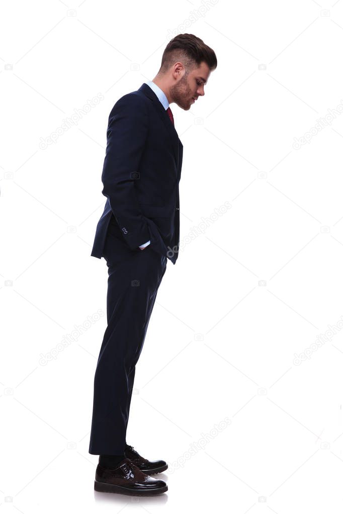 young businessman waiting in line looks down at something while standing on white background with hands in pockets, full body picture