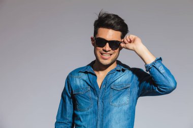 ışık gri arka plan üzerinde duran güneş gözlüklerini sabitleme mutlu casual adam portresi