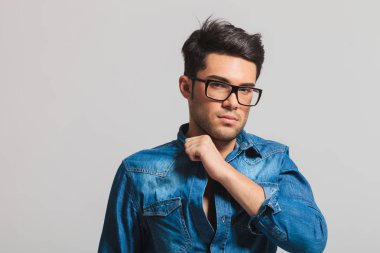 Genç akıllı casual adam açık gri renkli üzerinde dururken göğsünde elini tutarak gözlük ile portresi