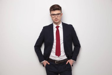 elleri ceplerinde ışık gey arka plan üzerinde duran rahat genç işadamı portresi