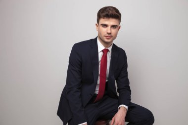 Lacivert takım elbiseli seksi genç işadamı ahşap açık gri renkli, portre resim taburede oturur