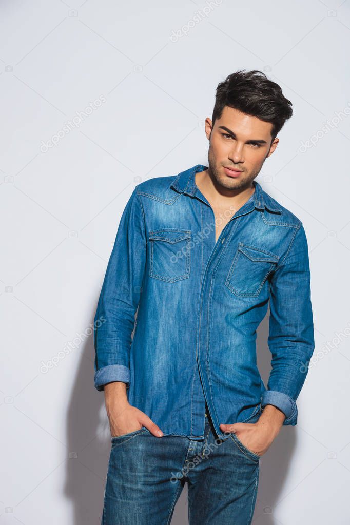 sexy young man wearing denim clothes standing on light grey background with hands in pockets