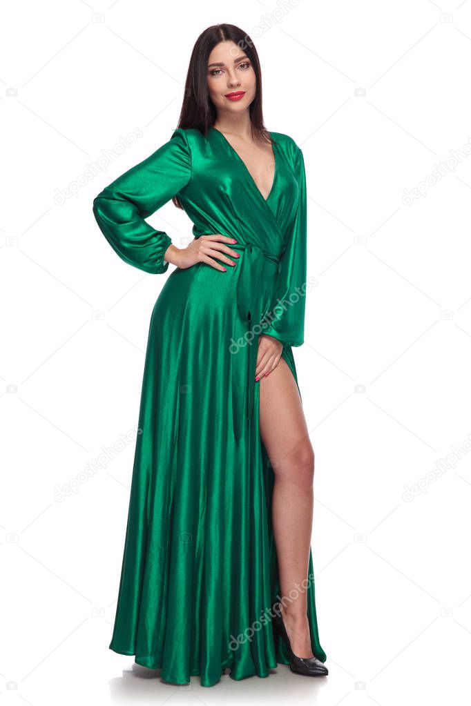 young brunette woman wearing an elegant green dress standing on white background with her hand on hip, full body picture
