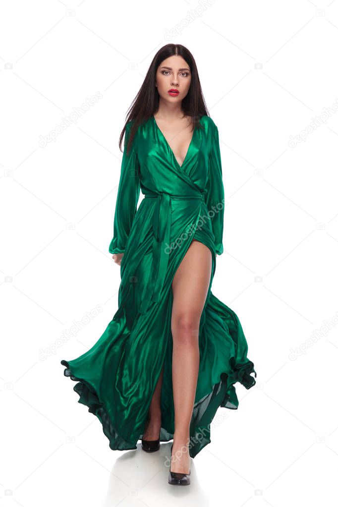 sexy woman wearing a long green fluttering dress walking forward on white background, full length picture