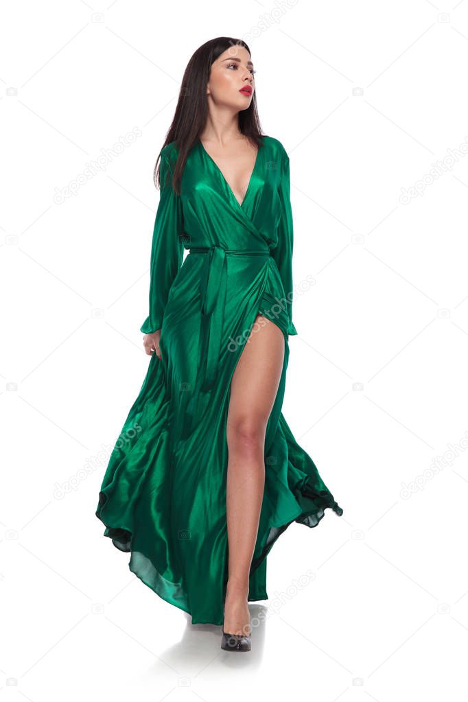 beautiful brunette woman wearing a green gown stepping on white background and looking to side, full length picture