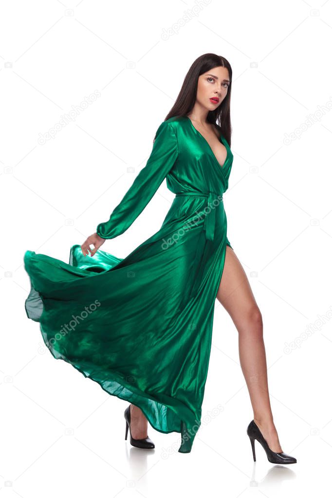 sexy woman in flying long green dress steps to side on white background, full length picture