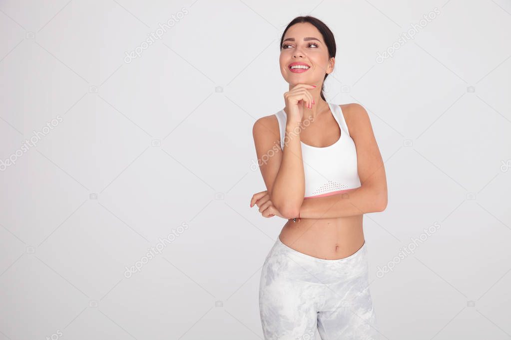 portrait of pensive fit woman looking to side while standing on light grey background