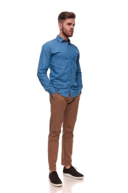 mavi tişört giyiyor rahat rahat adam ile elleri ceplerinde beyaz arka plan üzerinde duruyor ve tarafına, tam vücut resim görünüyor